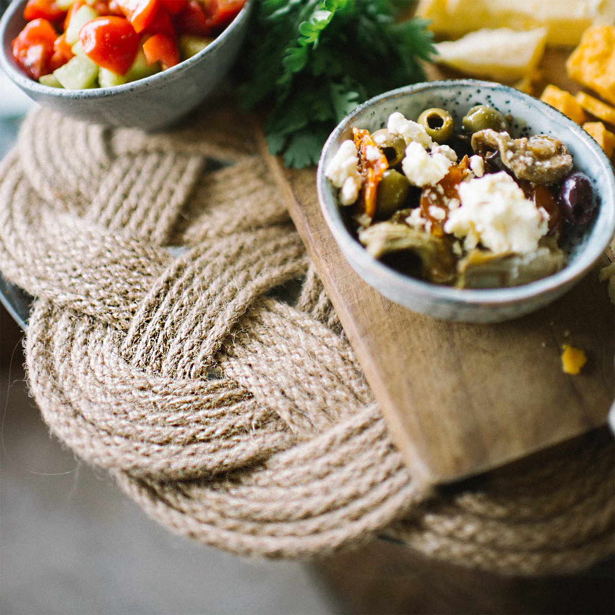 Mediterranean appetizer bowls with feta, olives, tomatoes on a braided rope mat