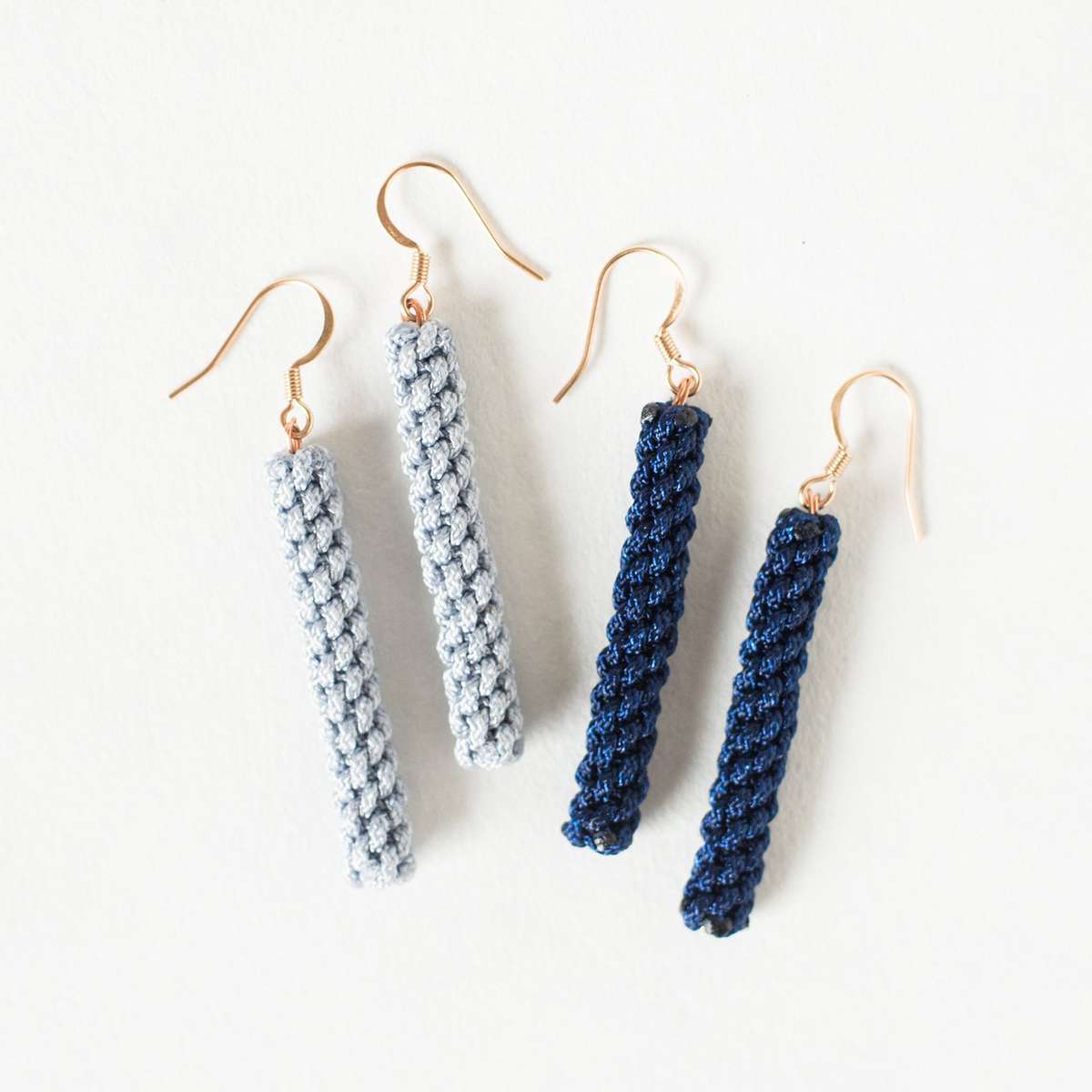 Two pairs of crochet dangle earrings in light blue and navy with gold hooks on white background