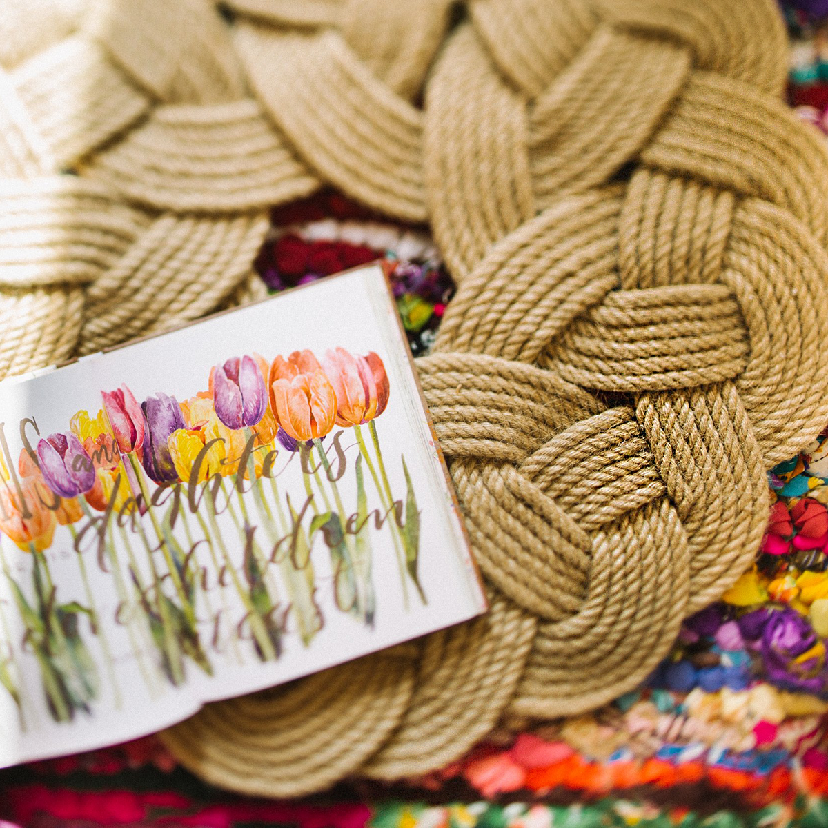 Braided jute rope mat and open floral watercolor book on colorful woven rug