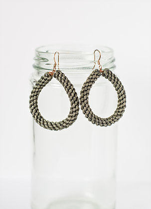 Braided metallic teardrop earrings displayed on a glass jar, minimal jewelry product photo